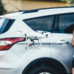 A woman flying a drone in front of her car